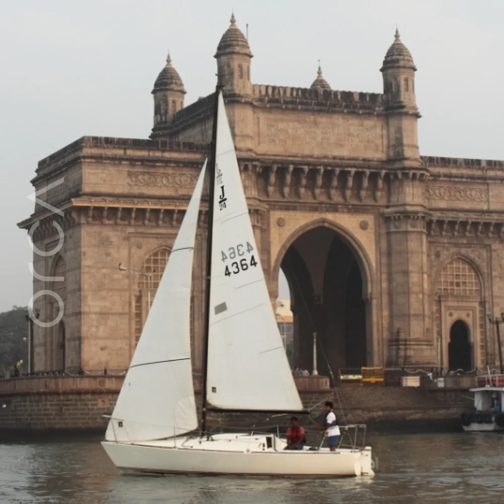 A J24 sailboat under sail at the Gateway of India in Mumbai, available to rent from Orca Sail.