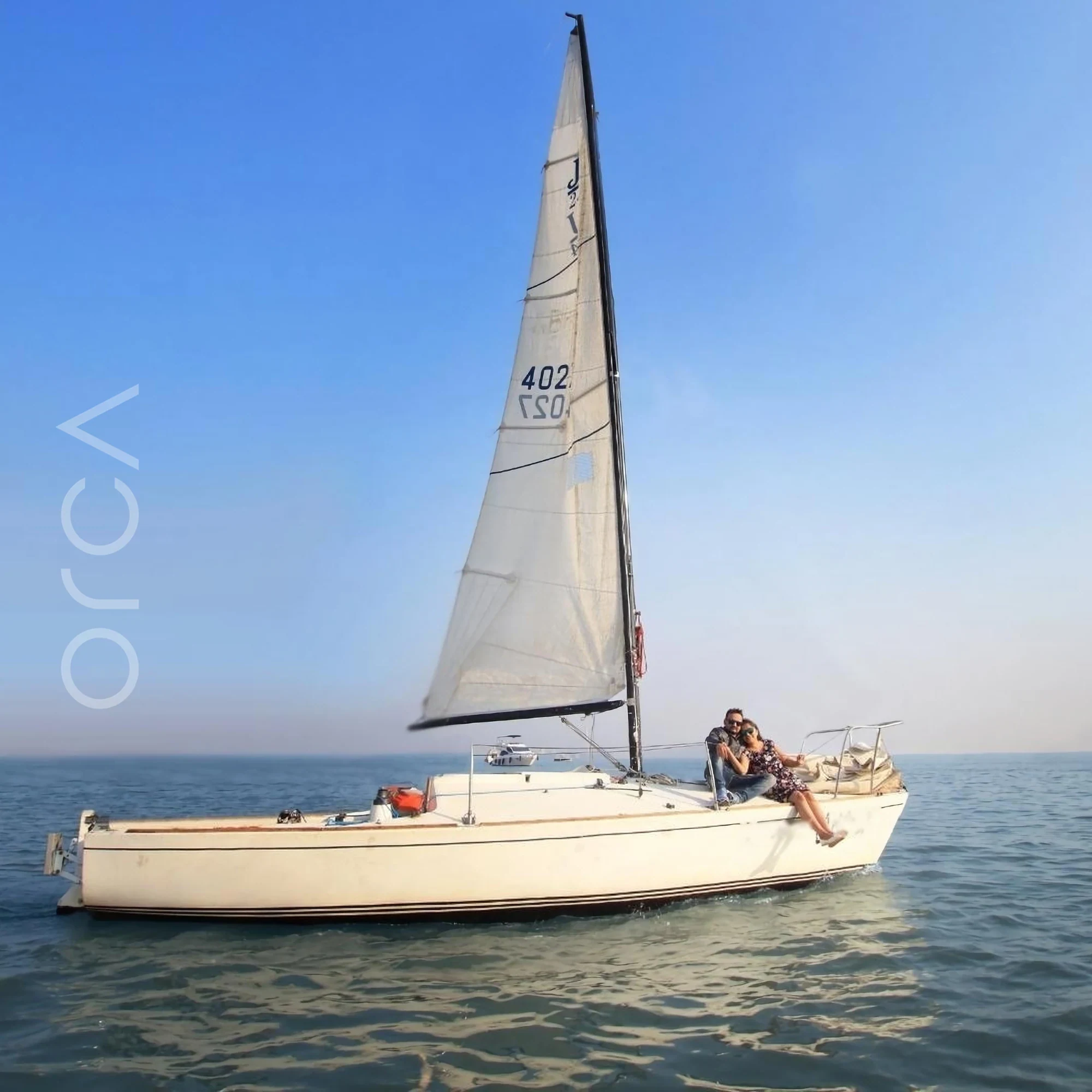 A J24 sailboat seen side-on off Mumbai with two guests at the bow, available to rent from Orca Sail.