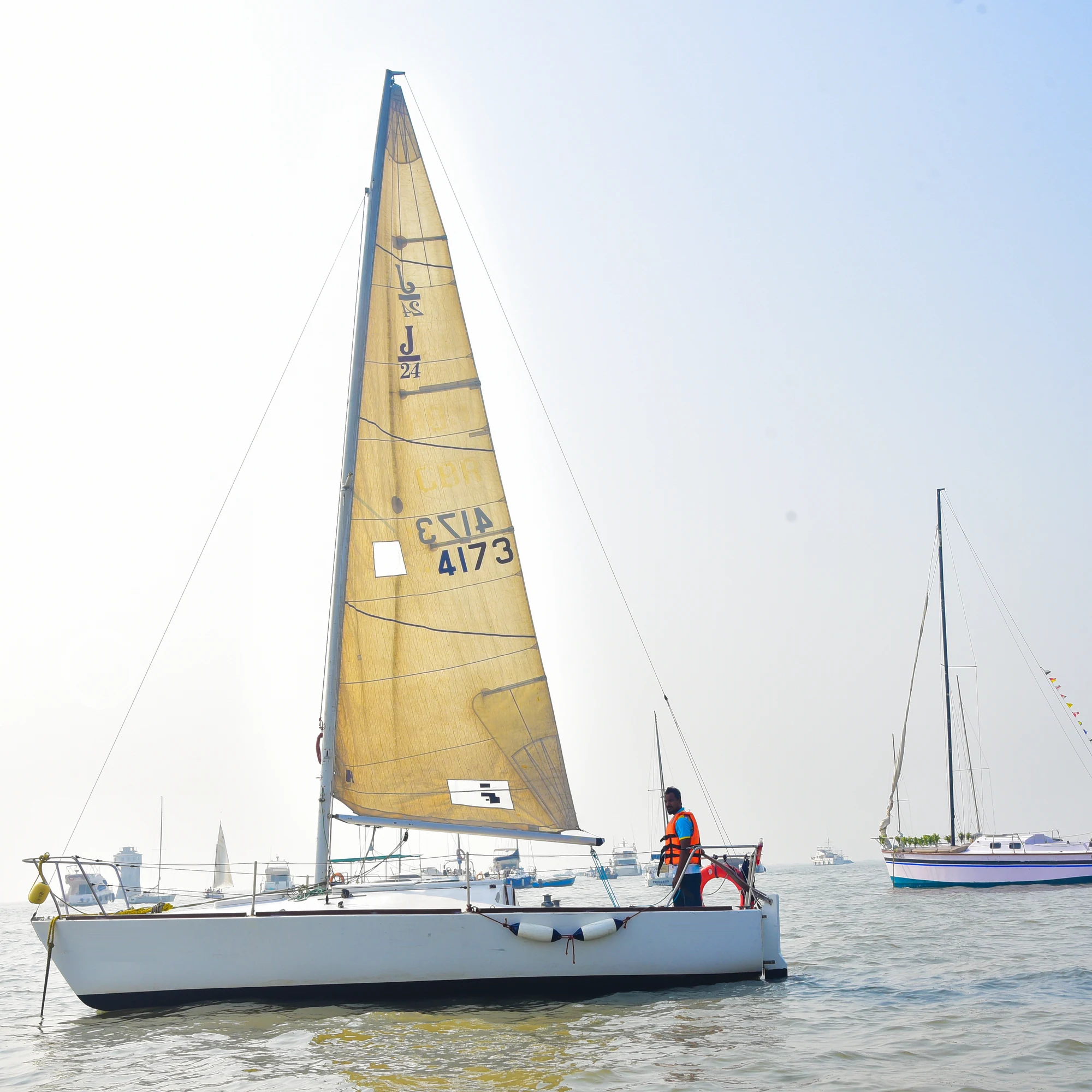 A side view of a J24 sailboat moored in Mumbai harbour, available to rent from Orca Sail.