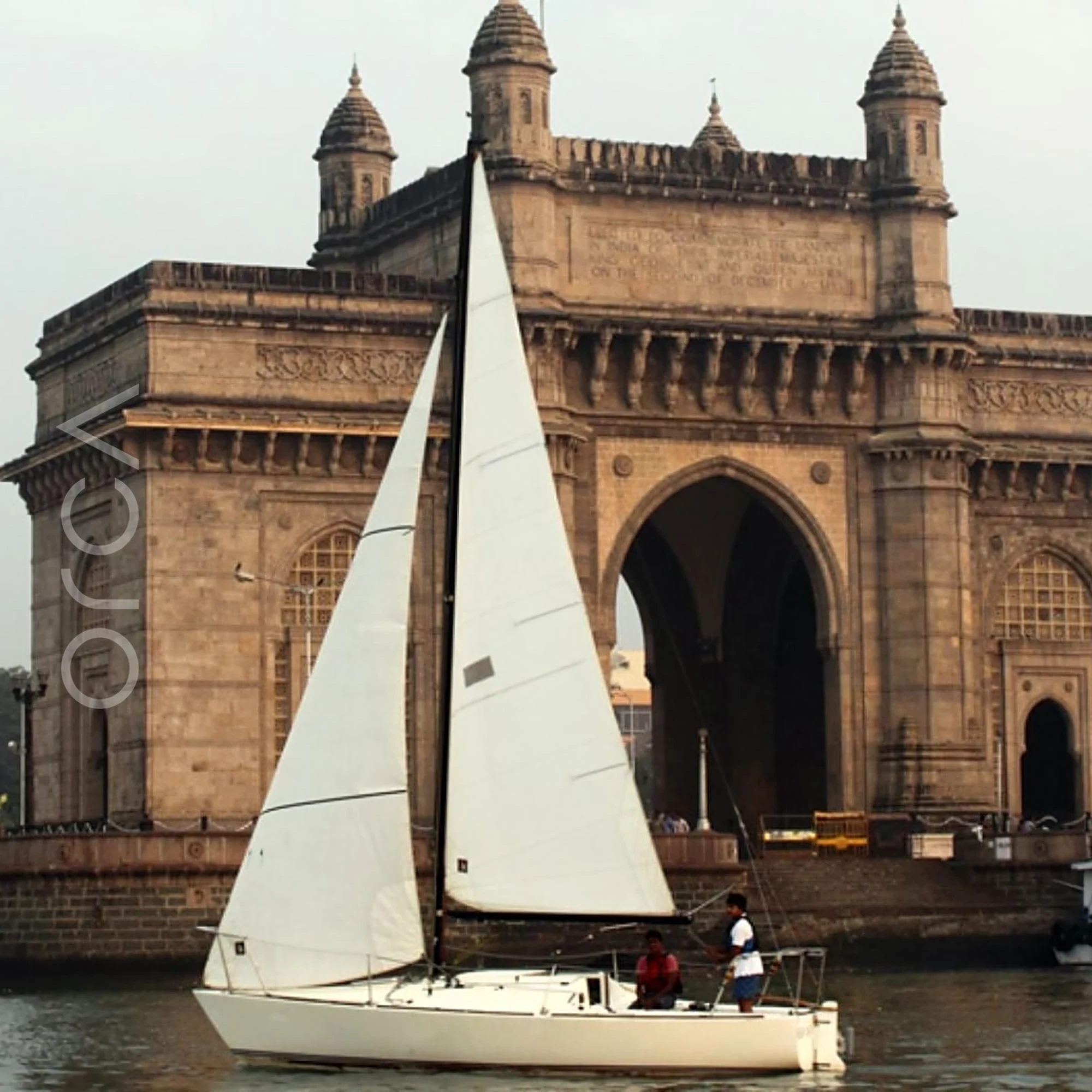 A J24 sailboat under sail at the Gateway of India in Mumbai, available to rent from Orca Sail.