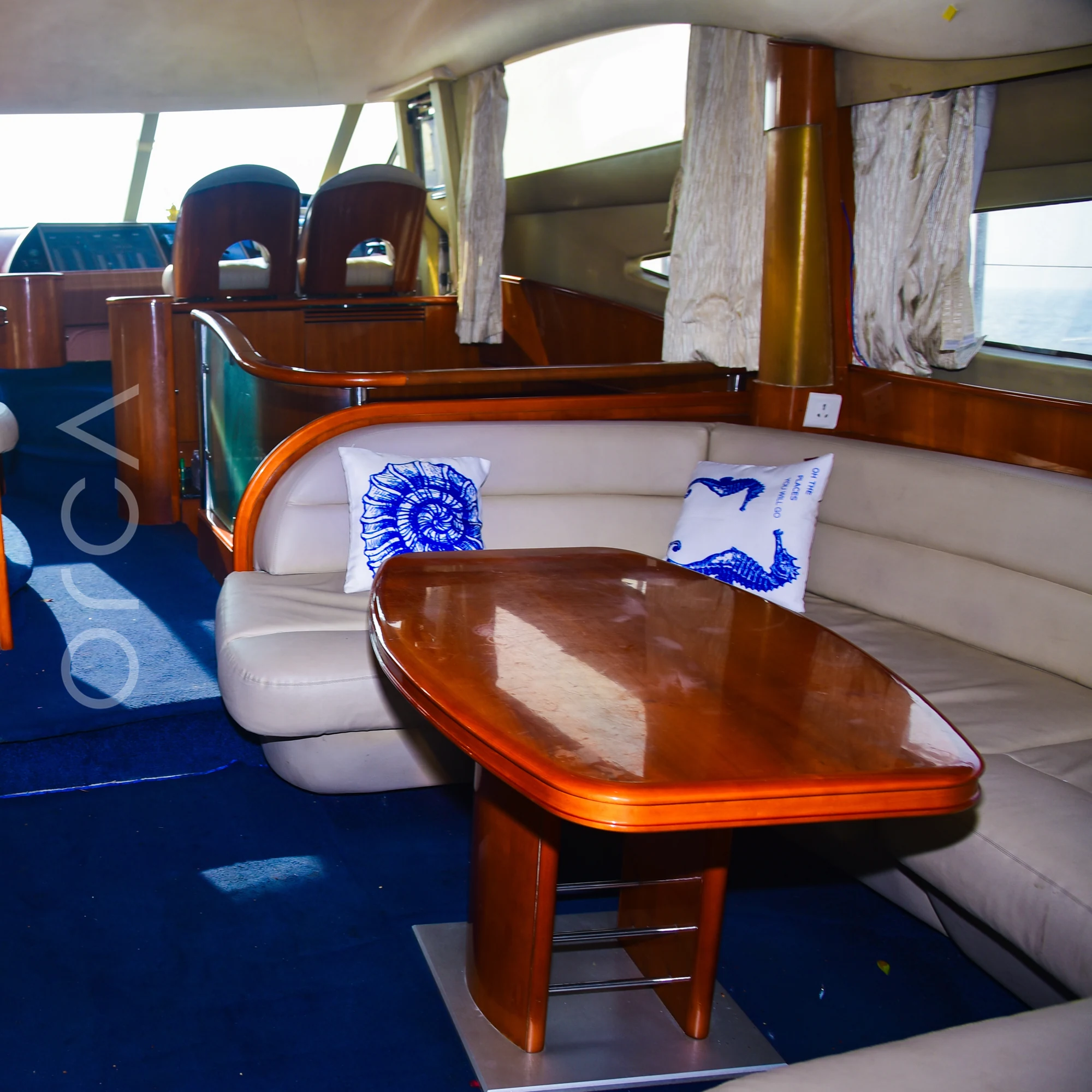 The main salon of a Princess 61 motor yacht in Mumbai, with a U-shaped sofa around a polished wood dining table and the lower helm beyond, available to rent from Orca Sail.