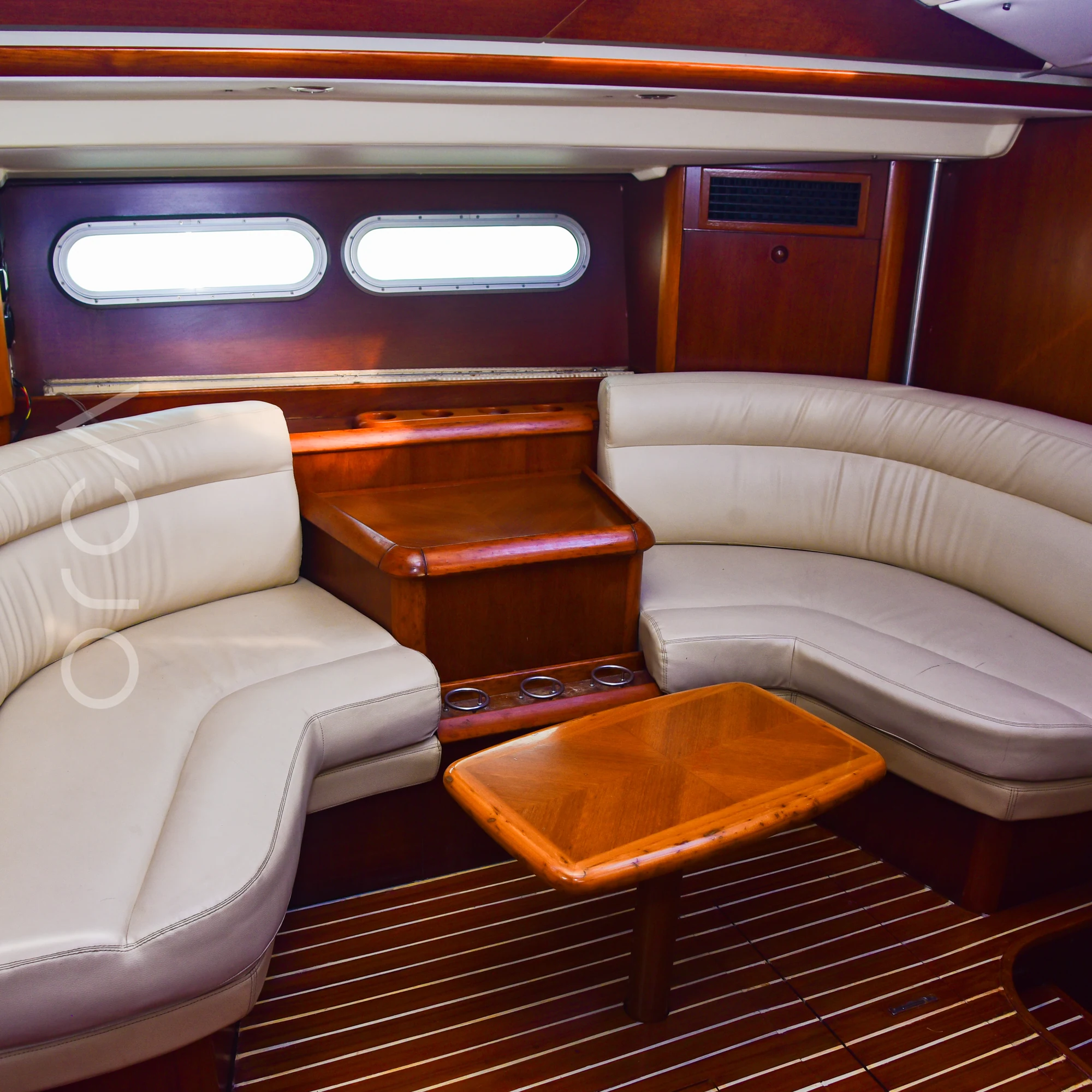 The main salon of a Jeanneau 54 sail yacht in Mumbai, with curved leather seating and a coffee table, available to rent from Orca Sail.