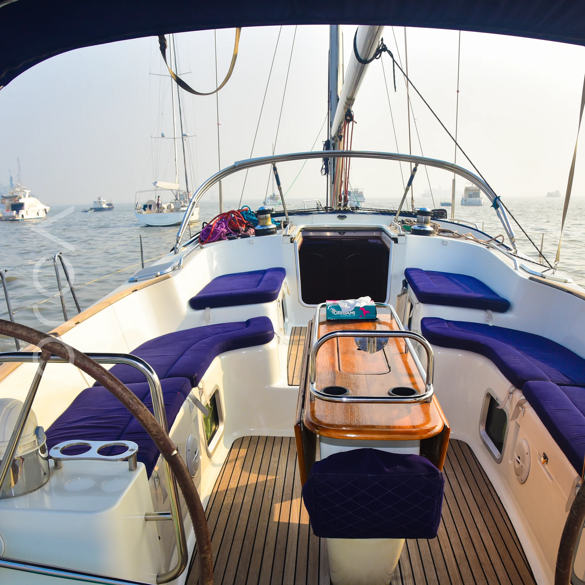 The cockpit of a Jeanneau 54 sail yacht in Mumbai, with cushioned seating and a table under the bimini, available to rent from Orca Sail.