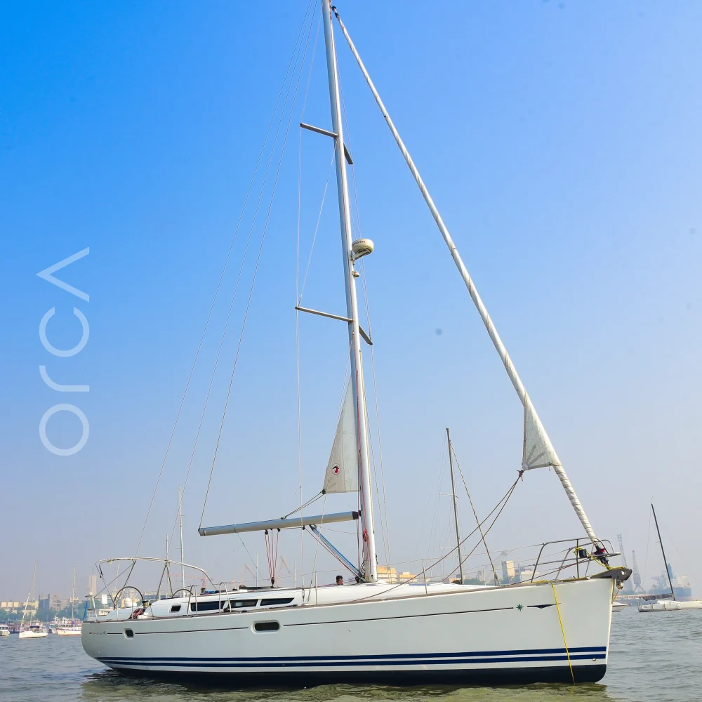The Jeanneau 45 sail yacht seen side-on at anchor in Mumbai harbour, the whole boat and mast in view, available to rent from Orca Sail.