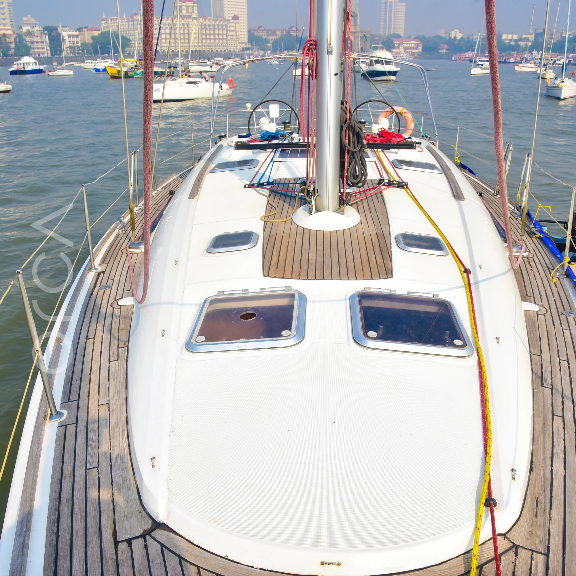 The foredeck of a Jeanneau 45 sail yacht in Mumbai, looking aft over the teak deck and hatches towards the mast and cockpit, available to rent from Orca Sail.