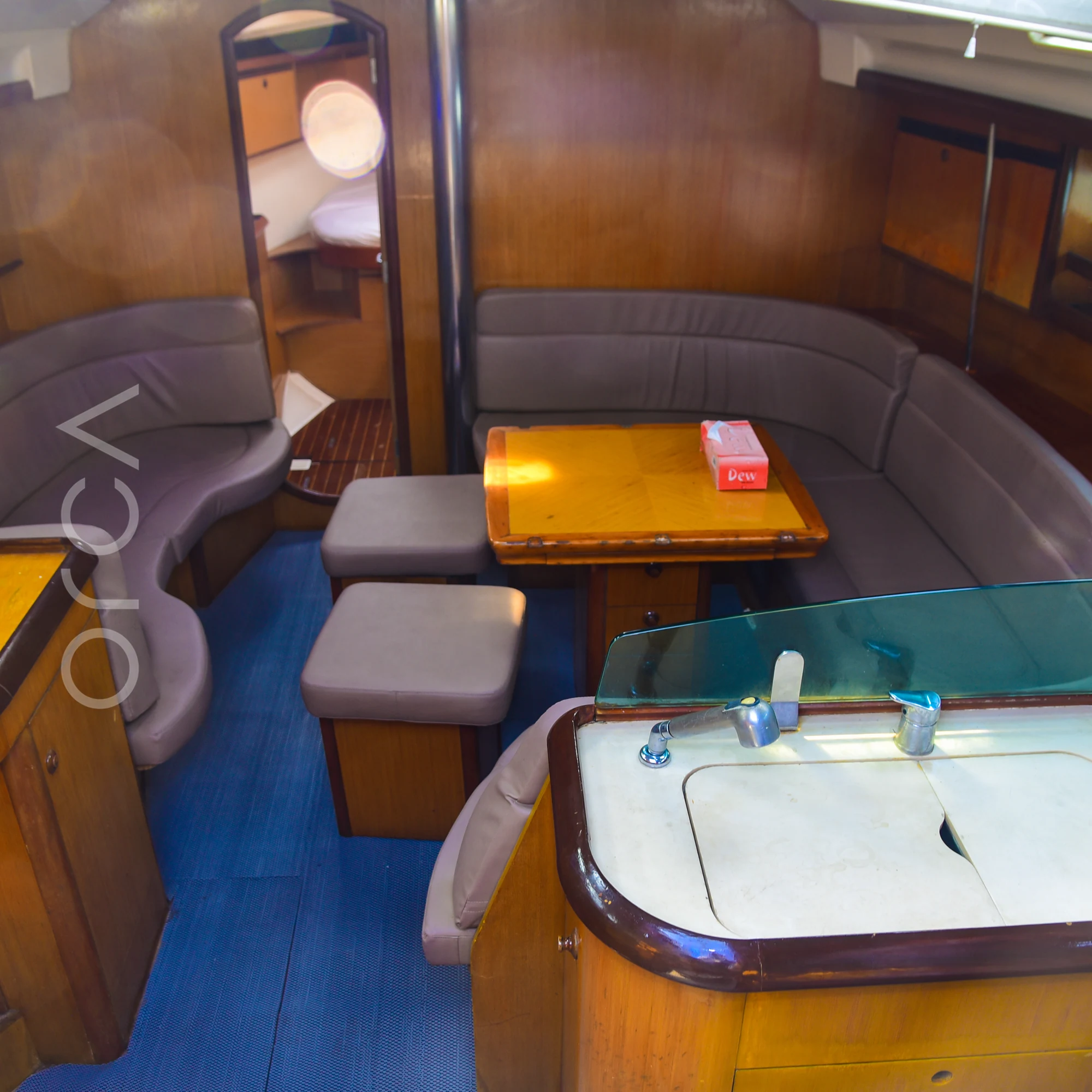 The main salon of a Jeanneau 45 sail yacht in Mumbai, with curved sofa seating, a table and the galley counter, available to rent from Orca Sail.