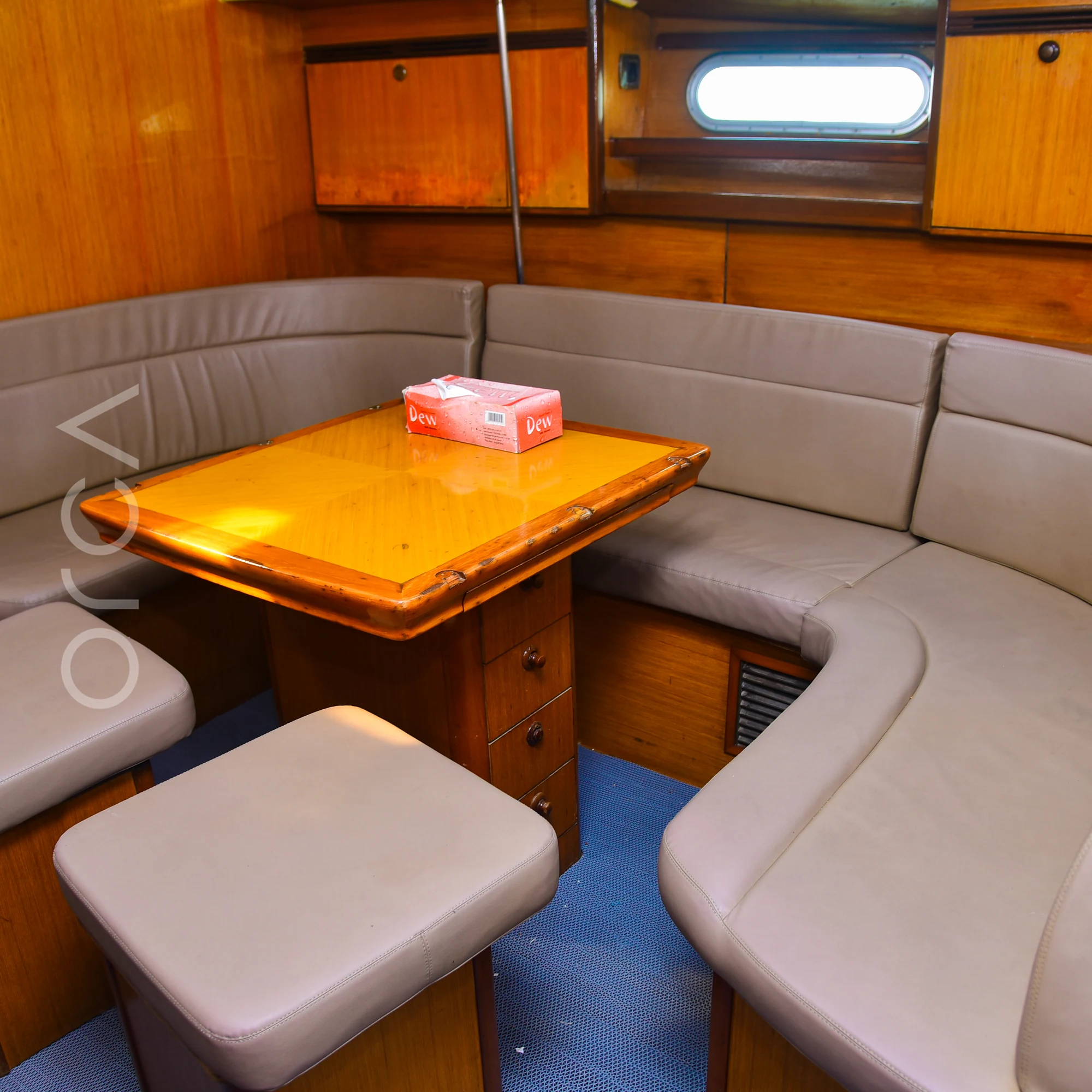The dining area of a Jeanneau 45 sail yacht in Mumbai, with U-shaped seating around a wooden table, available to rent from Orca Sail.