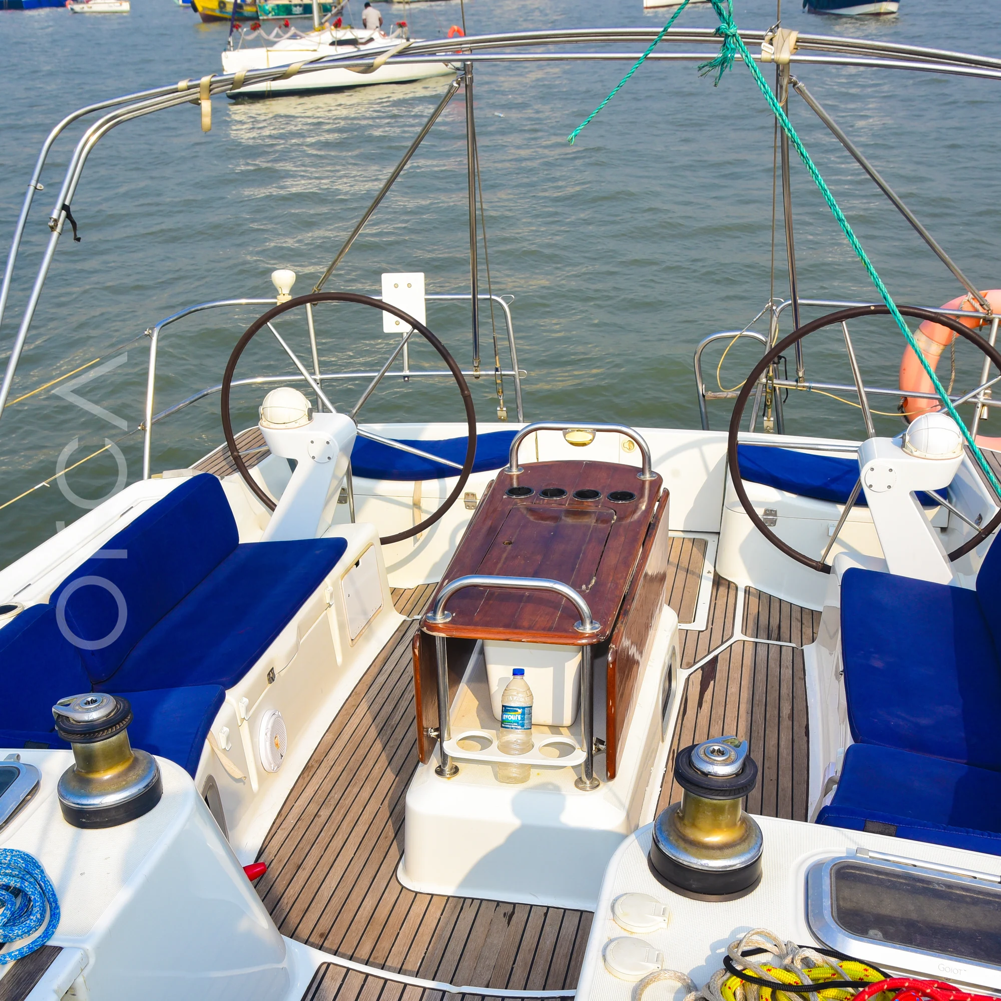 The cockpit of a Jeanneau 45 sail yacht in Mumbai harbour, with twin helm wheels, blue cushioned seating and a folding table, available to rent from Orca Sail.